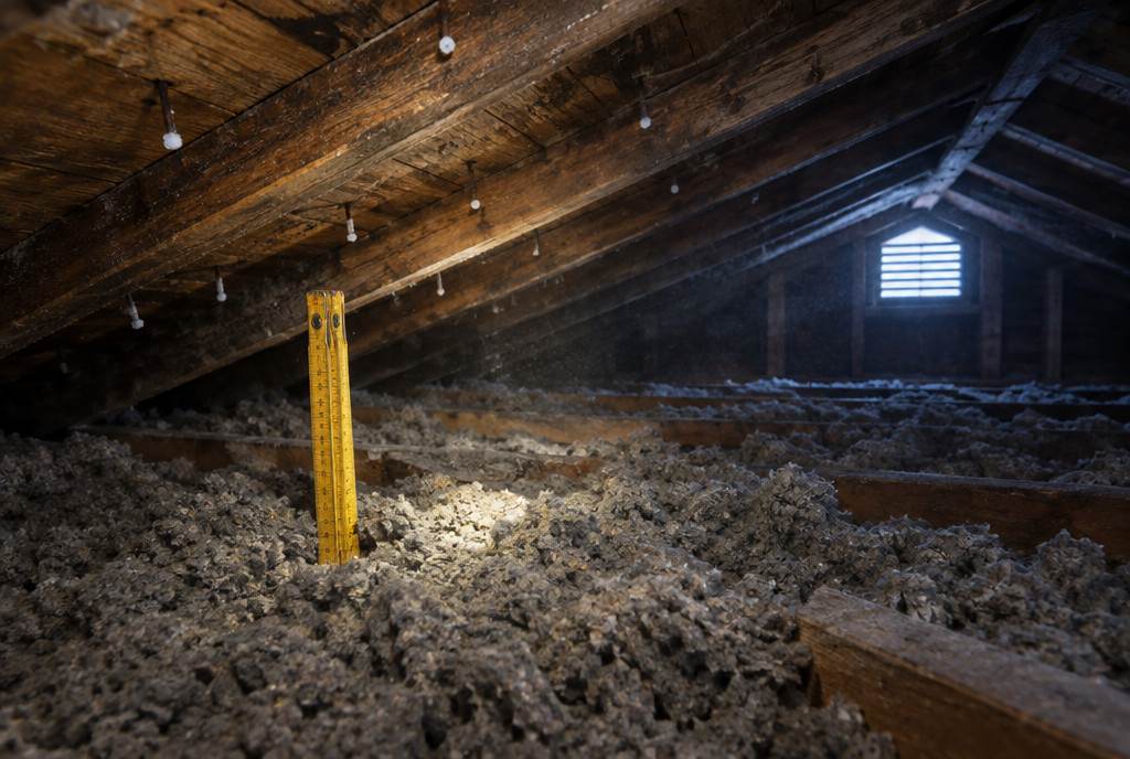 Loose-fill insulation between attic joists, a yellow ruler showing its depth and frost on the roofing nails above